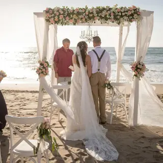 Beachfront wedding ceremony under a white gazebo with floral arrangements at Pueblo Bonito Rose, Cabo San Lucas