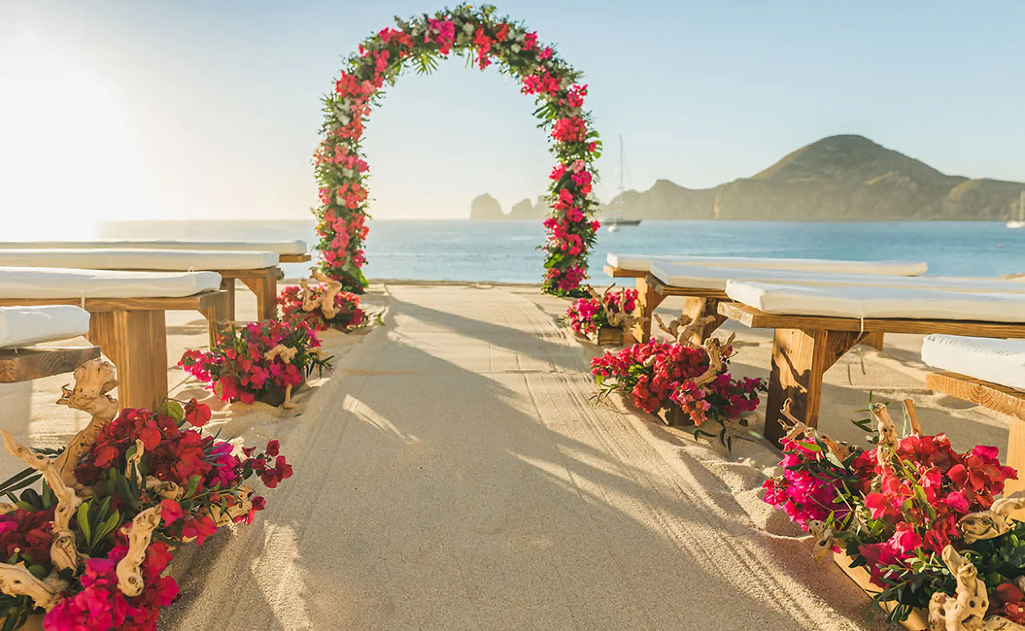 Beach wedding ceremony with a floral arch and wooden benches at Pueblo Bonito Rose, Cabo San Lucas