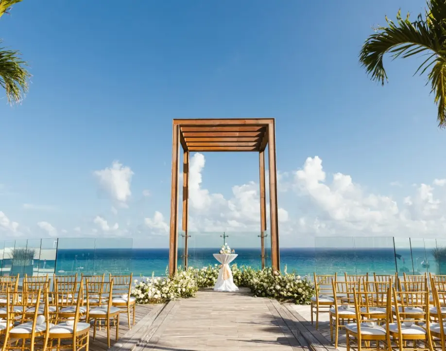 Oceanfront wedding ceremony setup with a wooden gazebo and gold chairs in Playa del Carmen
