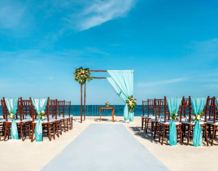 Beachfront wedding ceremony with light blue fabric décor and wooden chairs in Punta Cana