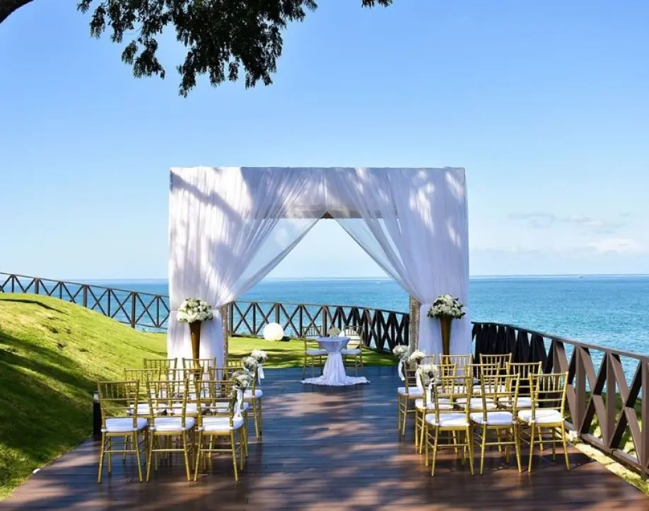Cliffside wedding ceremony setup with white drapery and gold chairs overlooking the ocean in Negril