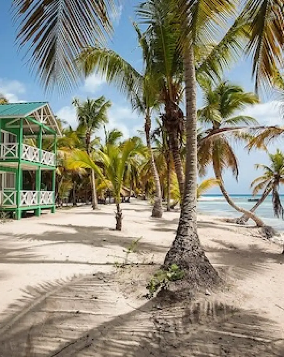 Green beachfront building and palm trees on the white sand in La Romana