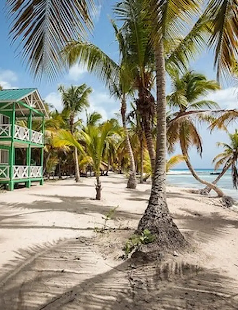 Green beachfront building and palm trees on the white sand in La Romana