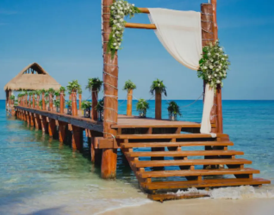 Wooden pier wedding ceremony venue with floral arch and white draping in Cozumel