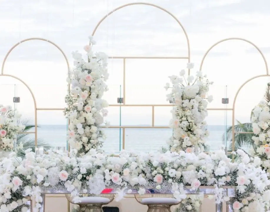 Oceanfront wedding reception setup with white flowers and golden arches in Playa del Carmen