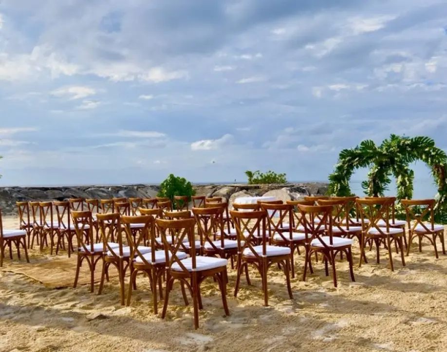 Beachfront wedding ceremony with wooden cross-back chairs and a circular greenery arch in Montego Bay