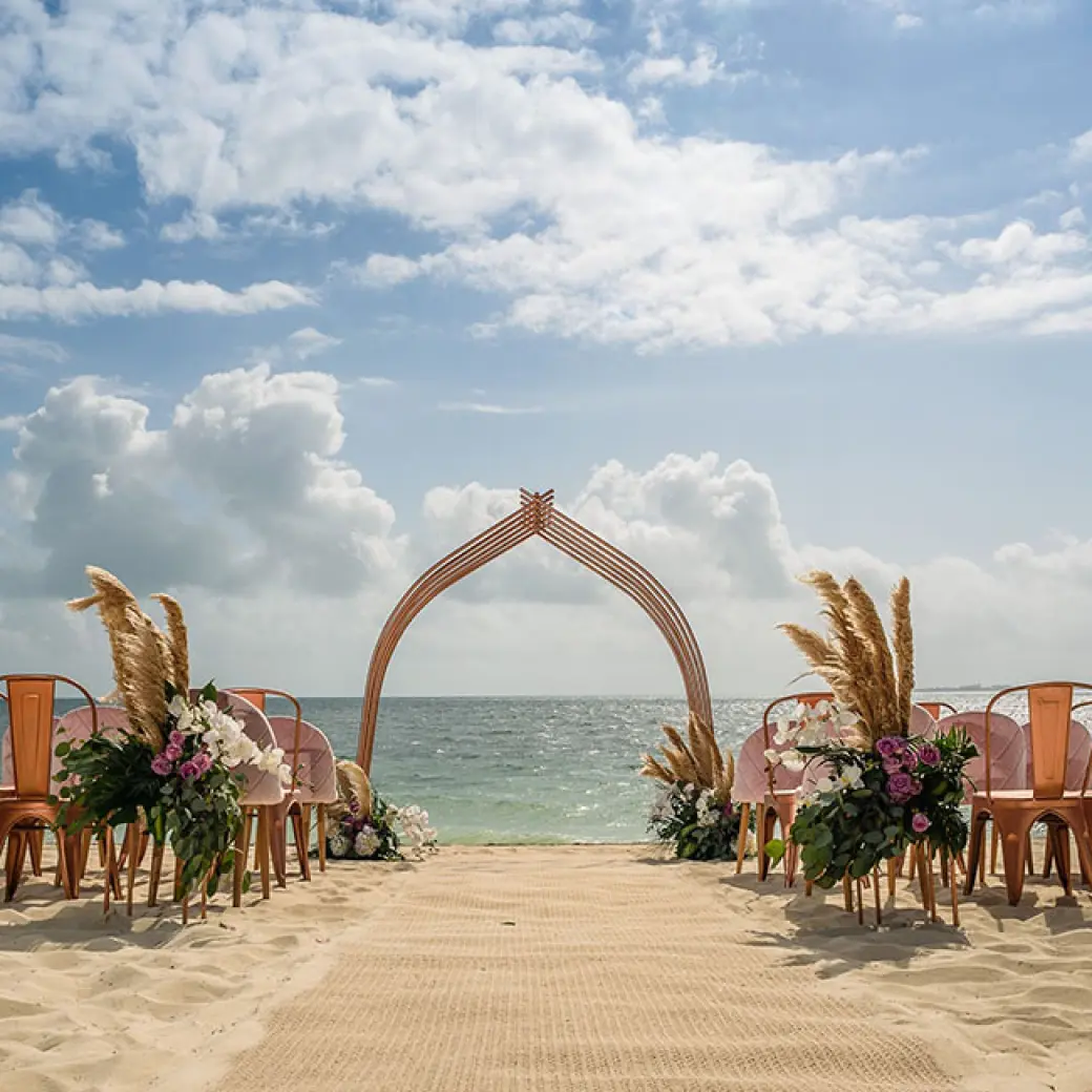 Beachfront wedding ceremony with a curved wooden arch and floral decor at Atelier Playa Mujeres, Cancun