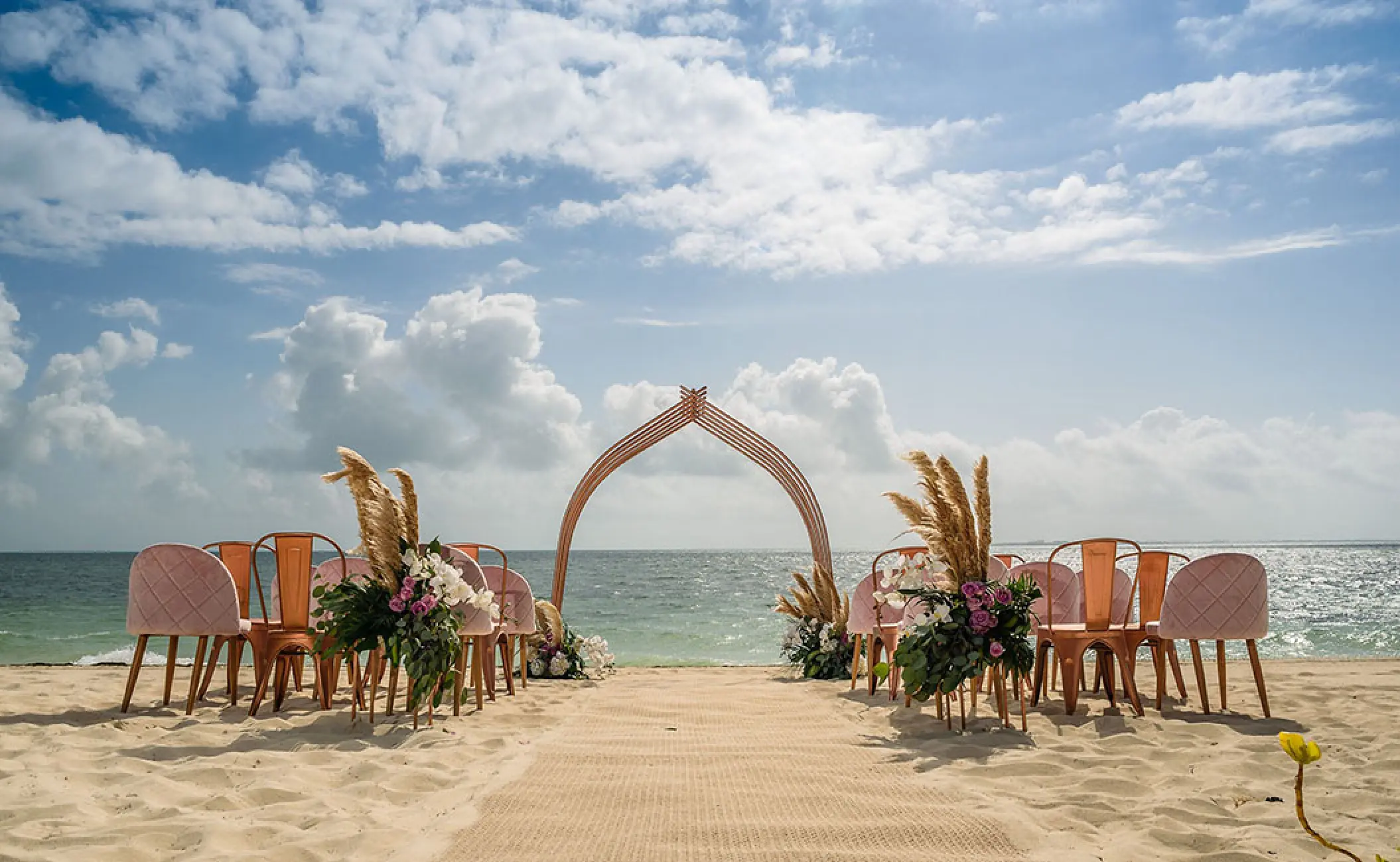 Beachfront wedding ceremony with a curved wooden arch and floral decor at Atelier Playa Mujeres, Cancun