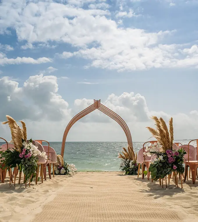 Beachfront wedding ceremony with a curved wooden arch and floral decor at Atelier Playa Mujeres, Cancun
