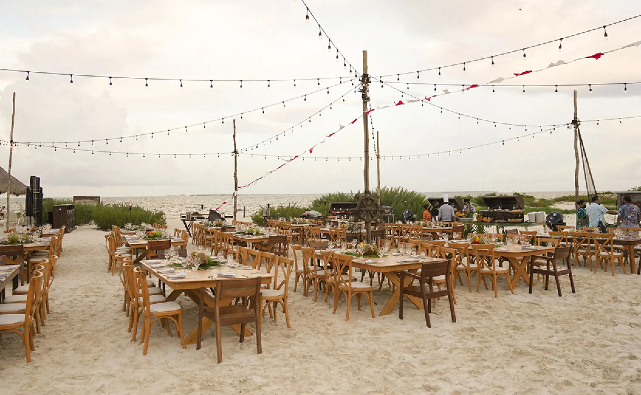 Beach wedding reception with wooden tables and string lights at Atelier Playa Mujeres, Cancun