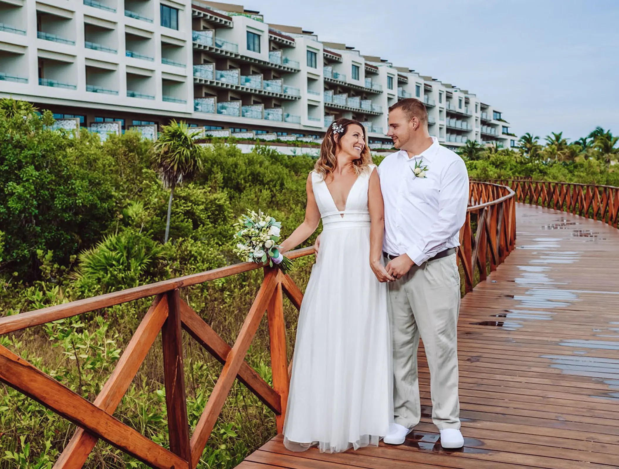 Bride and groom holding hands on a wooden boardwalk at Atelier Playa Mujeres, Cancun