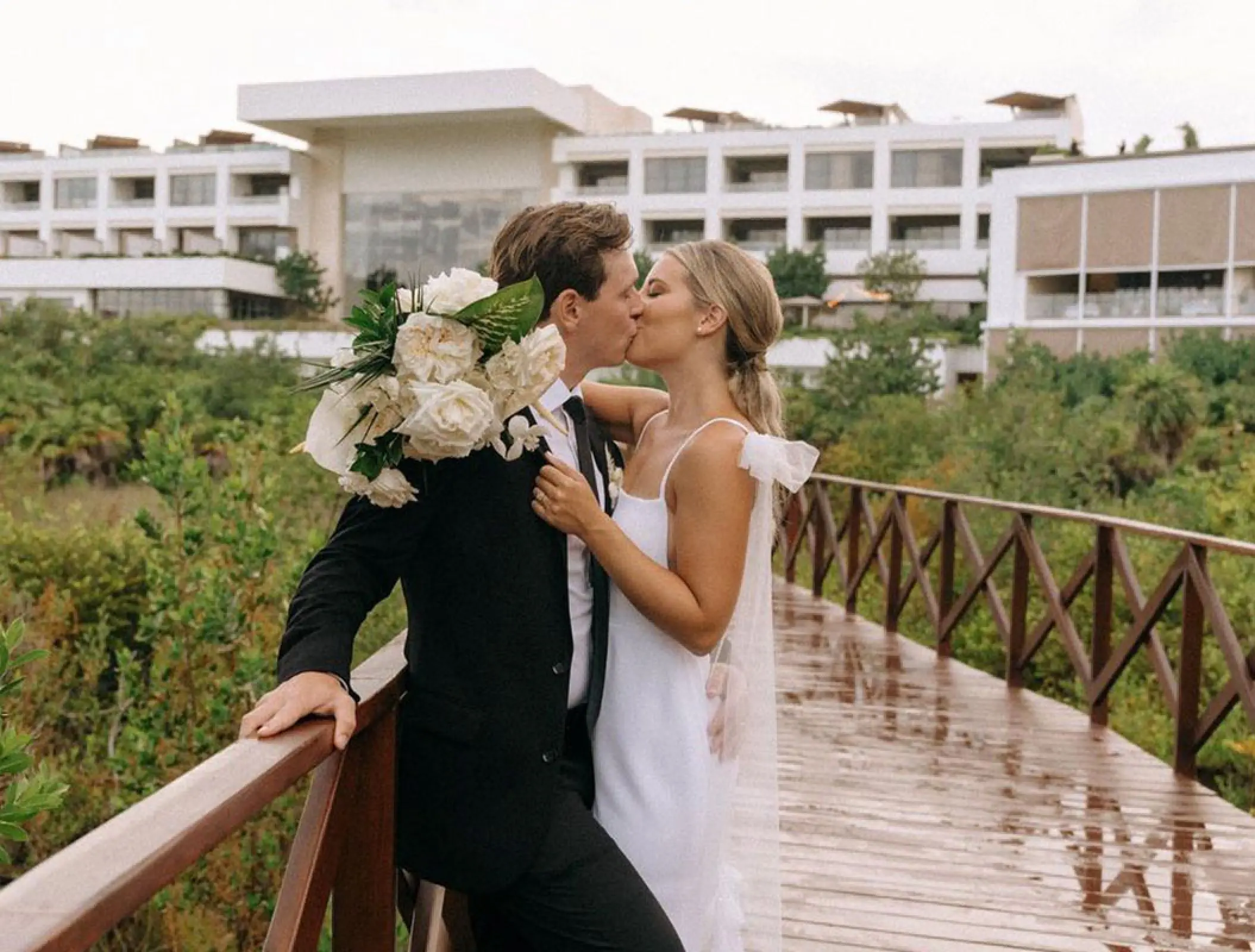 Bride and groom kissing on a wooden walkway at Atelier Playa Mujeres, Cancun