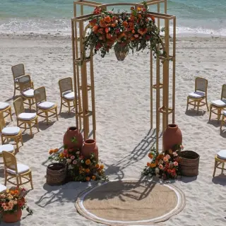 Beachfront wedding ceremony setup with wooden arch and orange floral arrangements at Atelier Playa Mujeres, Cancun
