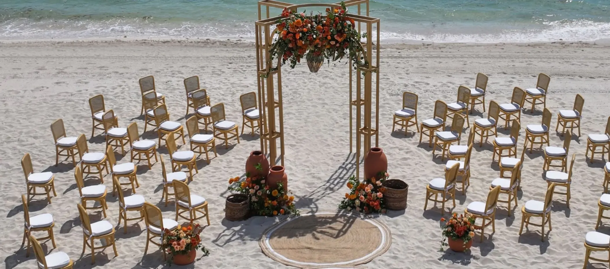 Beachfront wedding ceremony setup with wooden arch and orange floral arrangements at Atelier Playa Mujeres, Cancun