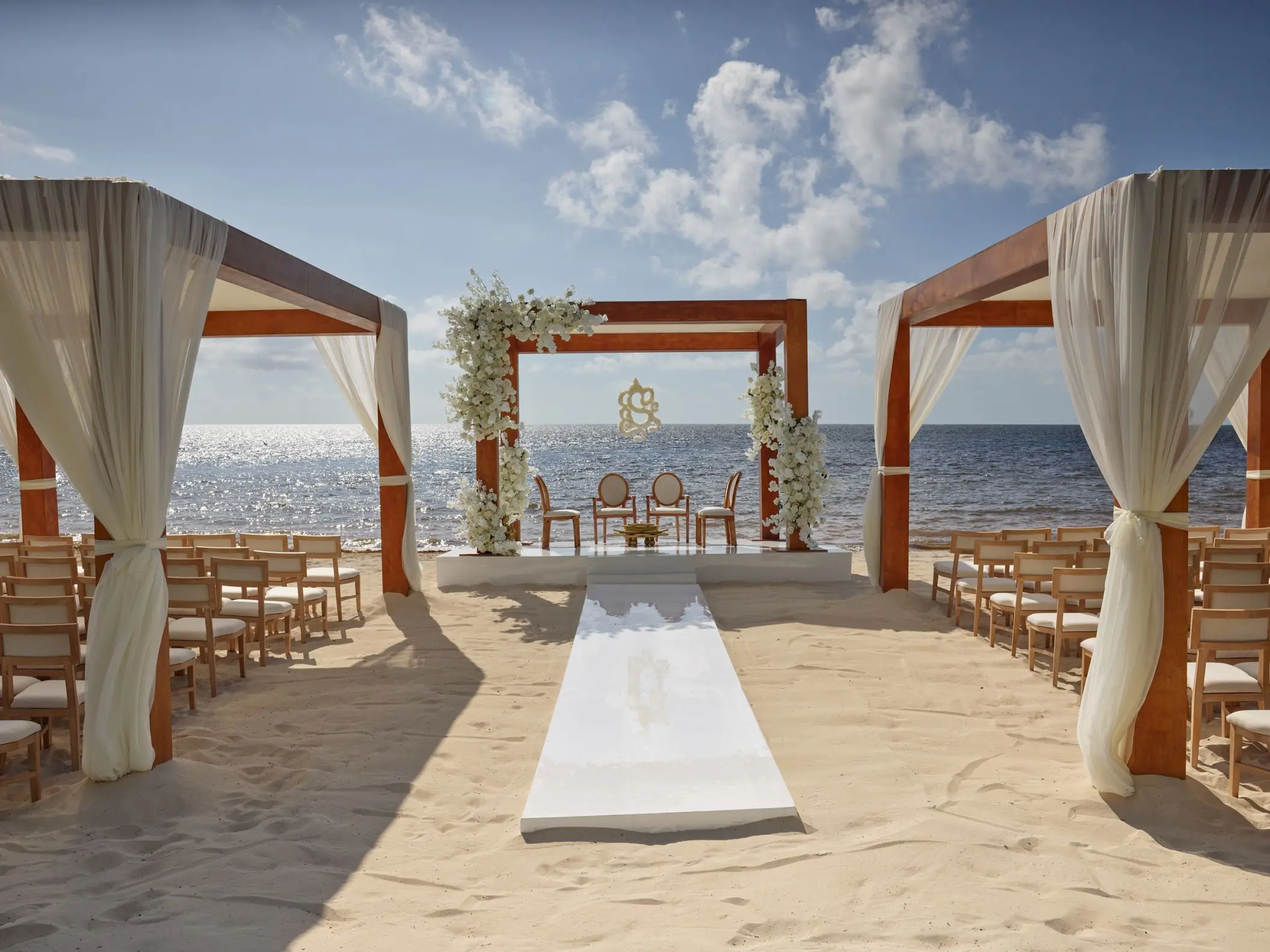 Beachfront wedding ceremony setup with wooden arches and white curtains at AVA Resort Cancun, Cancun