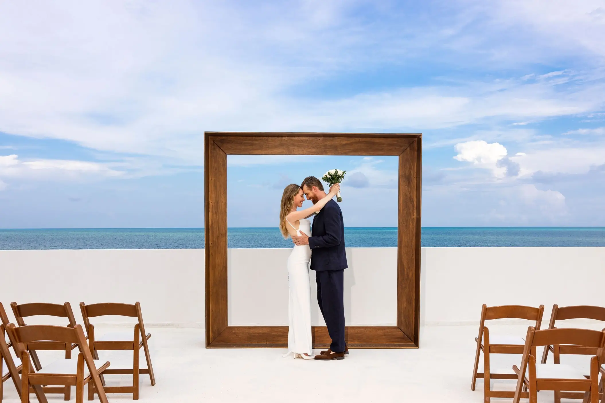 Bride and groom posing inside a wooden frame at a rooftop wedding ceremony at AVA Resort Cancun