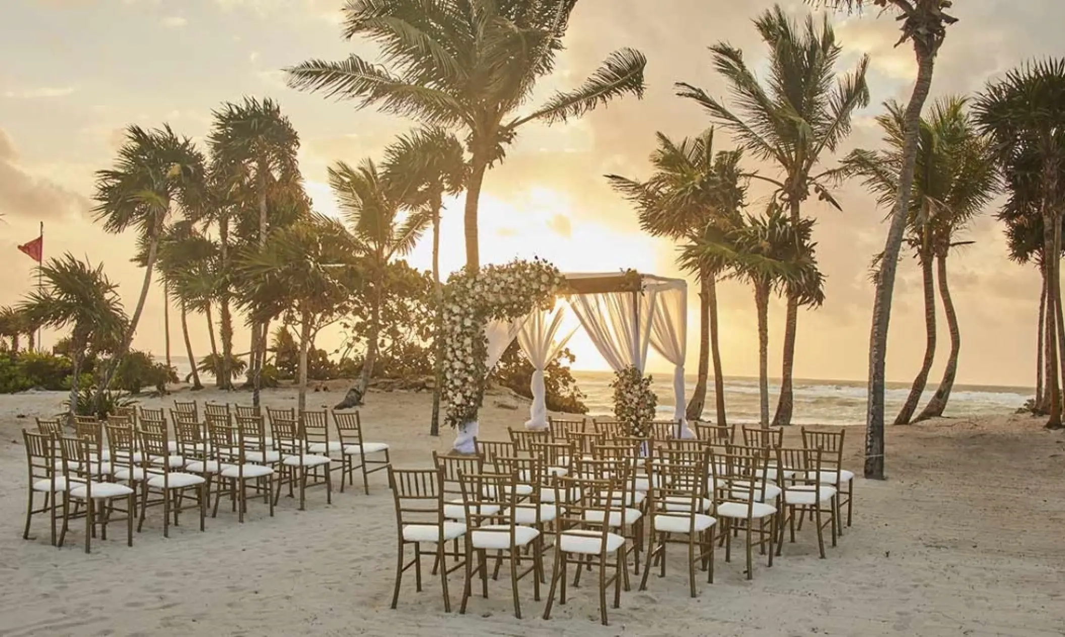Beachfront wedding ceremony with white huppa and gold chairs at Bahia Principe Grand Coba, Tulum