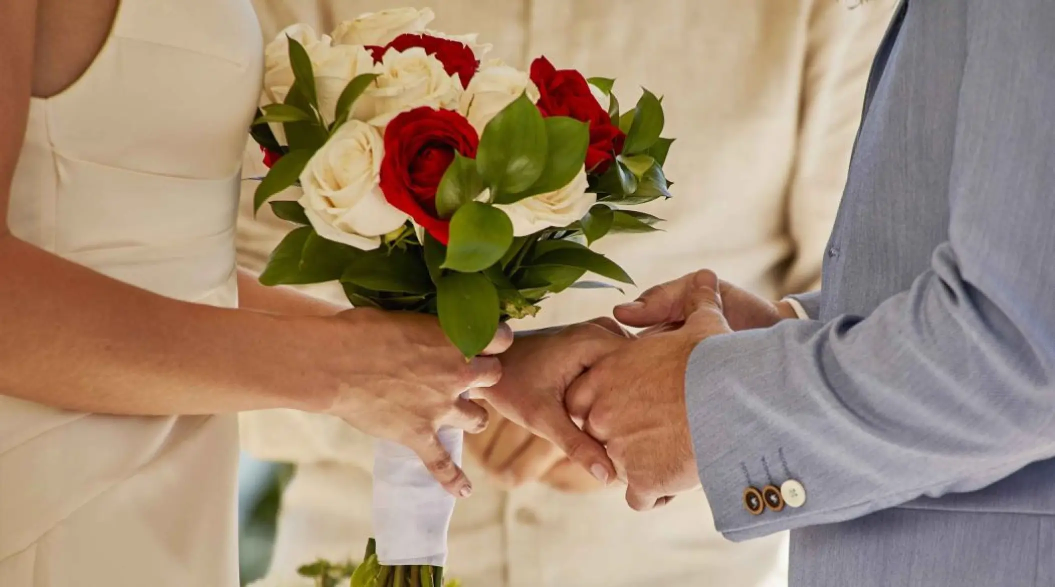 Close-up of a bride and groom holding hands with a rose bouquet at Bahia Principe Grand Coba, Tulum