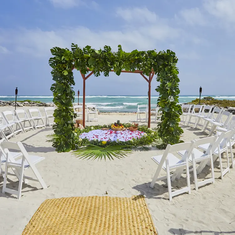 Beachfront wedding ceremony with greenery arch and circular seating at Bahia Principe Luxury Akumal, Tulum