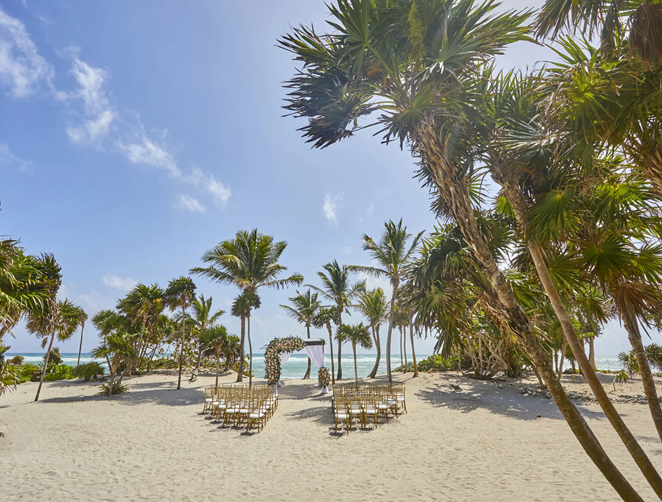 Beachfront wedding ceremony with a floral arch and gold chairs at Bahia Principe Akumal, Tulum