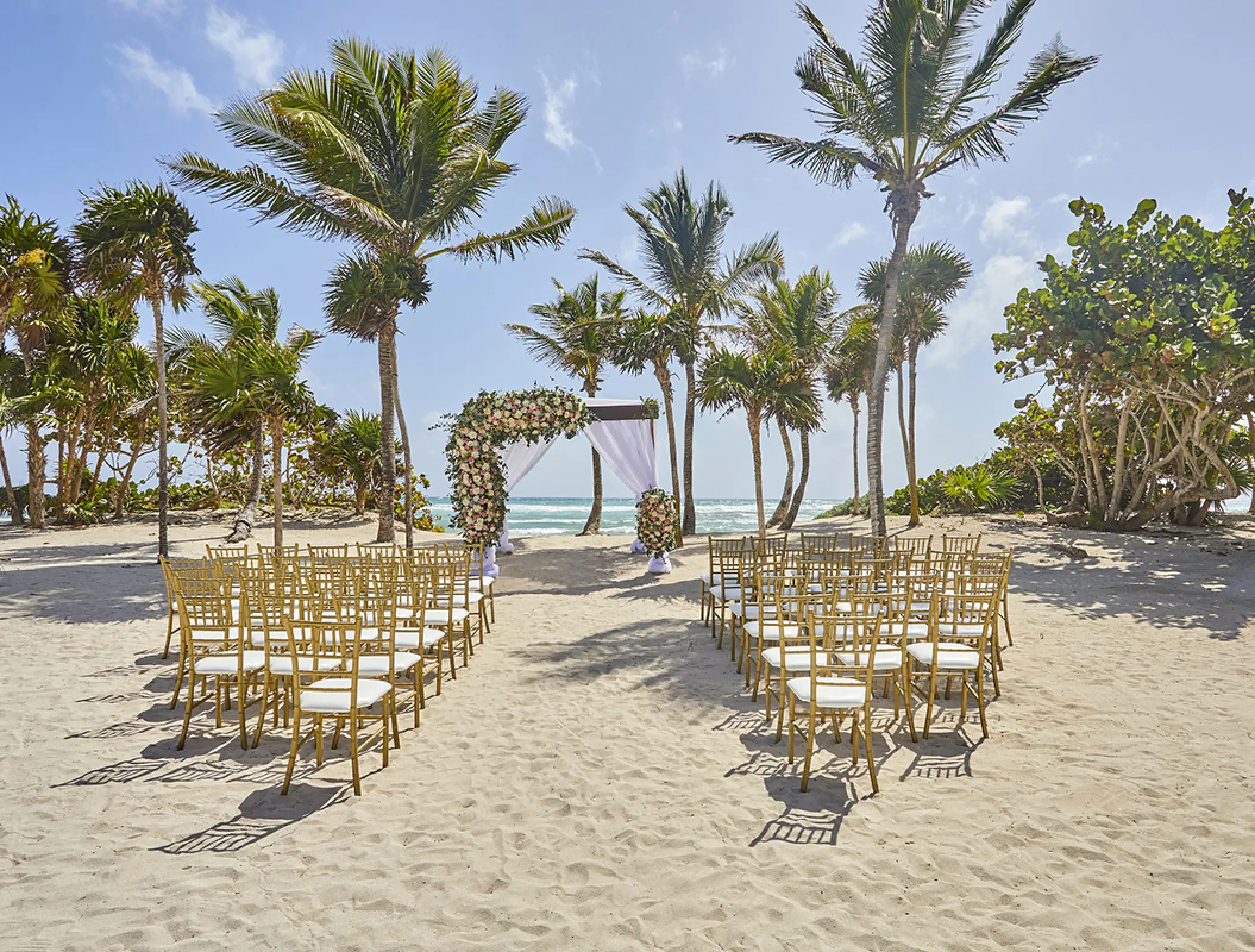 Beachfront wedding ceremony with gold chairs and floral huppa at Bahia Principe Akumal, Tulum
