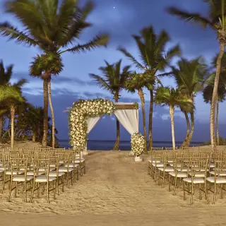 Beachfront wedding ceremony setup with white floral arch and gold chairs at Bahia Principe Akumal, Tulum