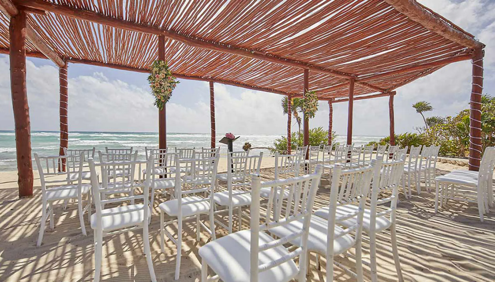 Shaded beach wedding ceremony setup under a wooden pergola at Bahia Principe Akumal, Tulum