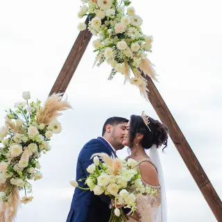 The bride and groom embracing under a triangle floral arch at Barcelo Puerto Vallarta, Puerto Vallarta
