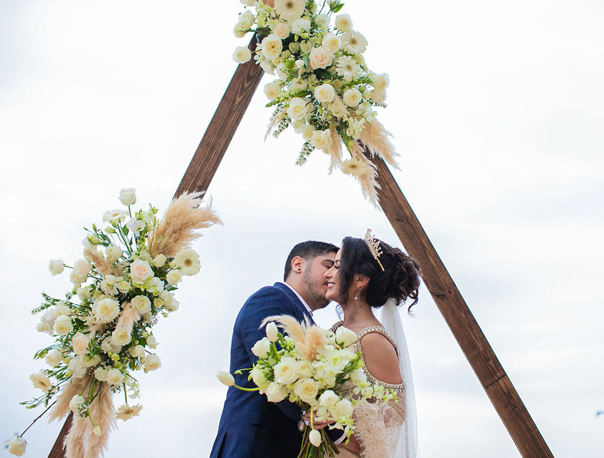 The bride and groom embracing under a triangle floral arch at Barcelo Puerto Vallarta, Puerto Vallarta