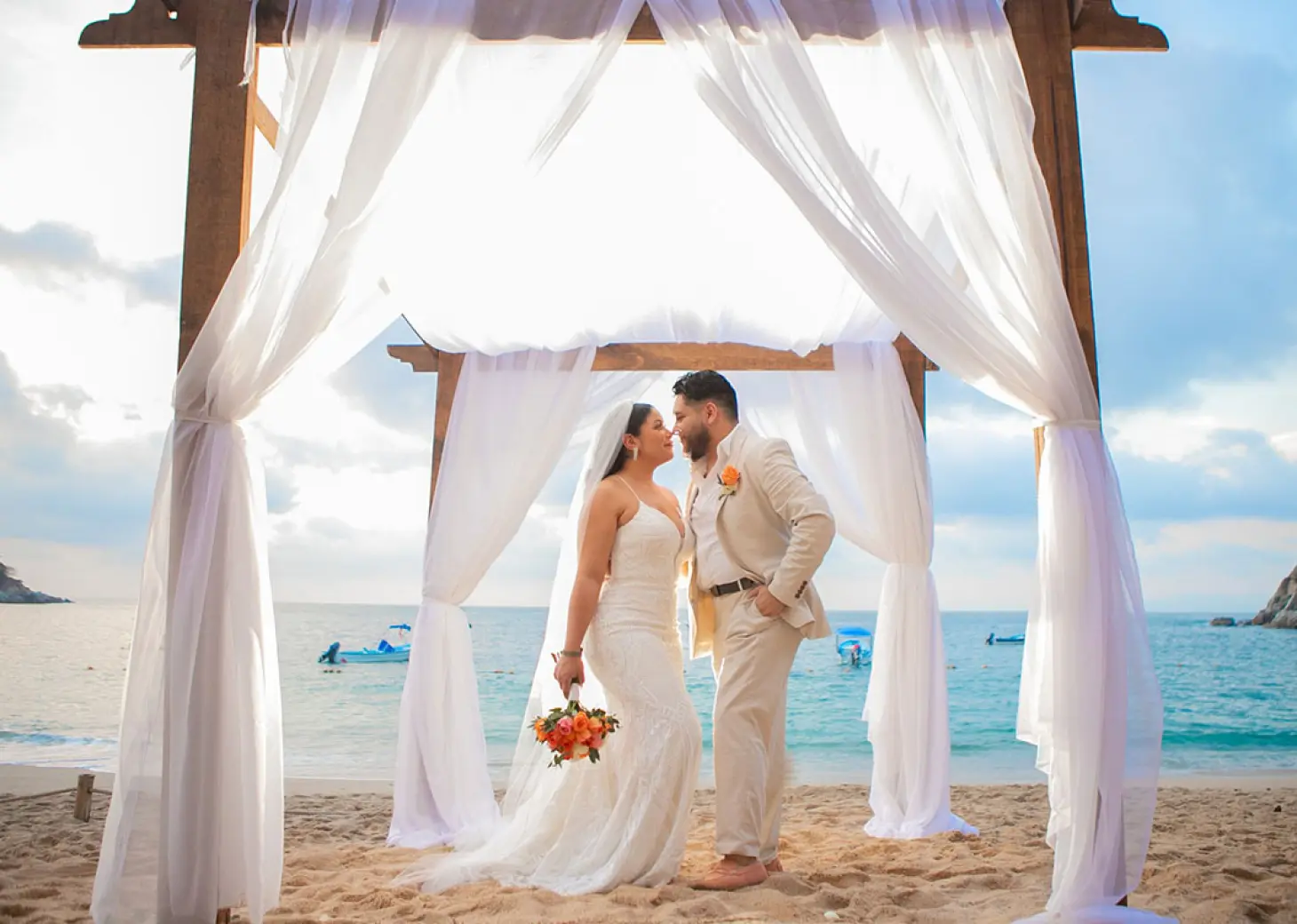 The bride and groom posing under a wooden arch for a beach ceremony at Barcelo Puerto Vallarta
