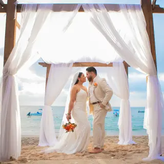 The bride and groom posing under a wooden arch for a beach ceremony at Barcelo Puerto Vallarta