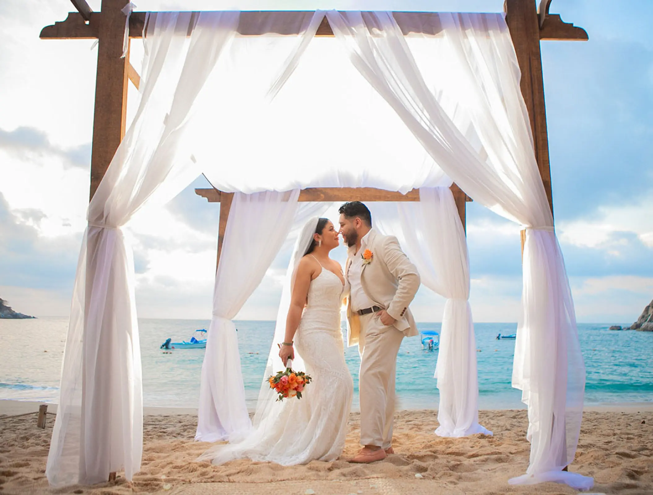 The bride and groom posing under a wooden arch for a beach ceremony at Barcelo Puerto Vallarta
