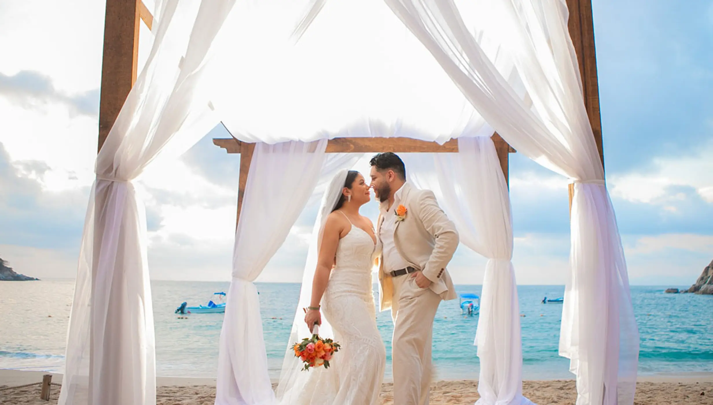 The bride and groom posing under a wooden arch for a beach ceremony at Barcelo Puerto Vallarta