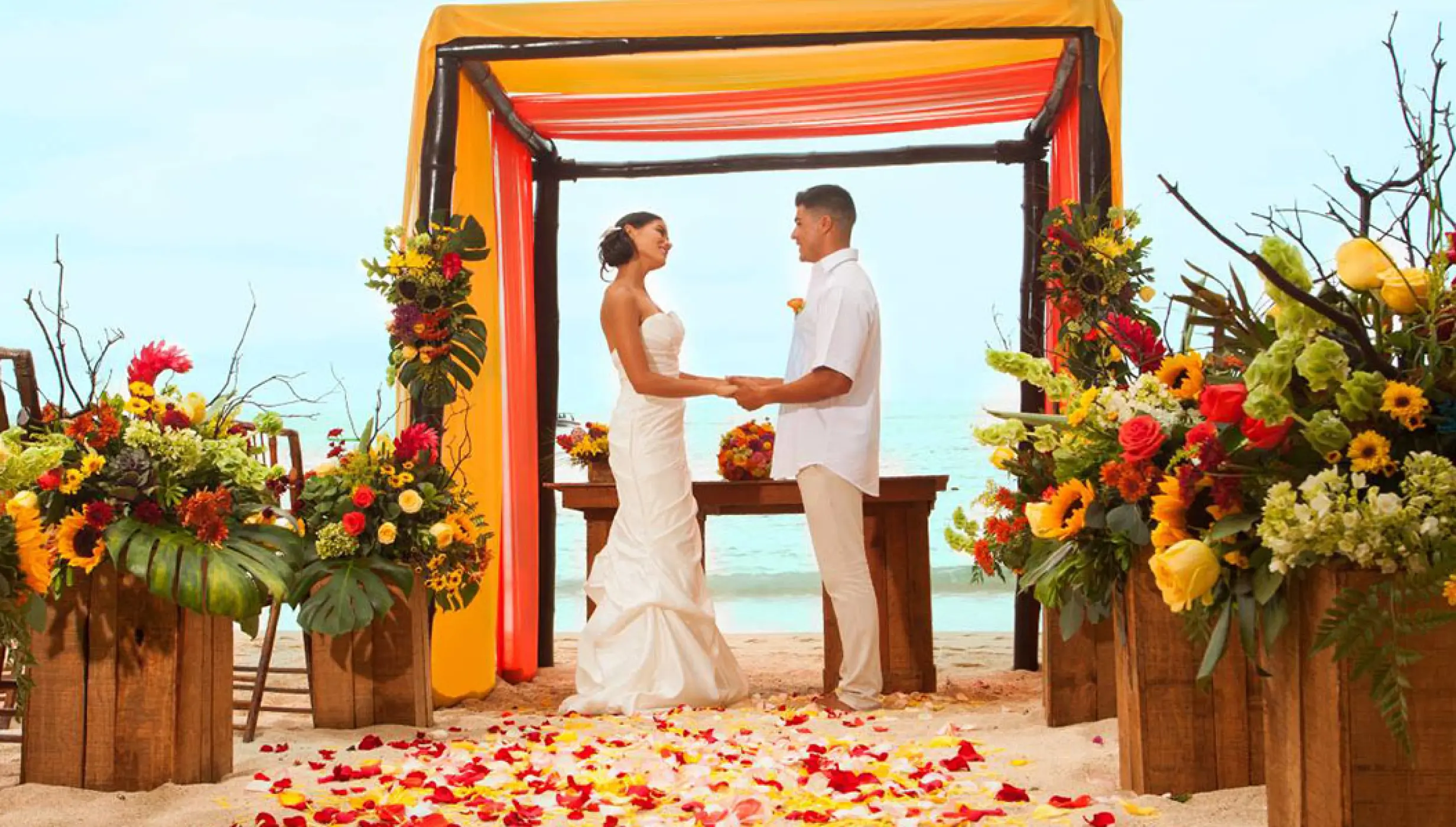 Beachfront wedding ceremony with yellow and orange floral decor at Barcelo Puerto Vallarta