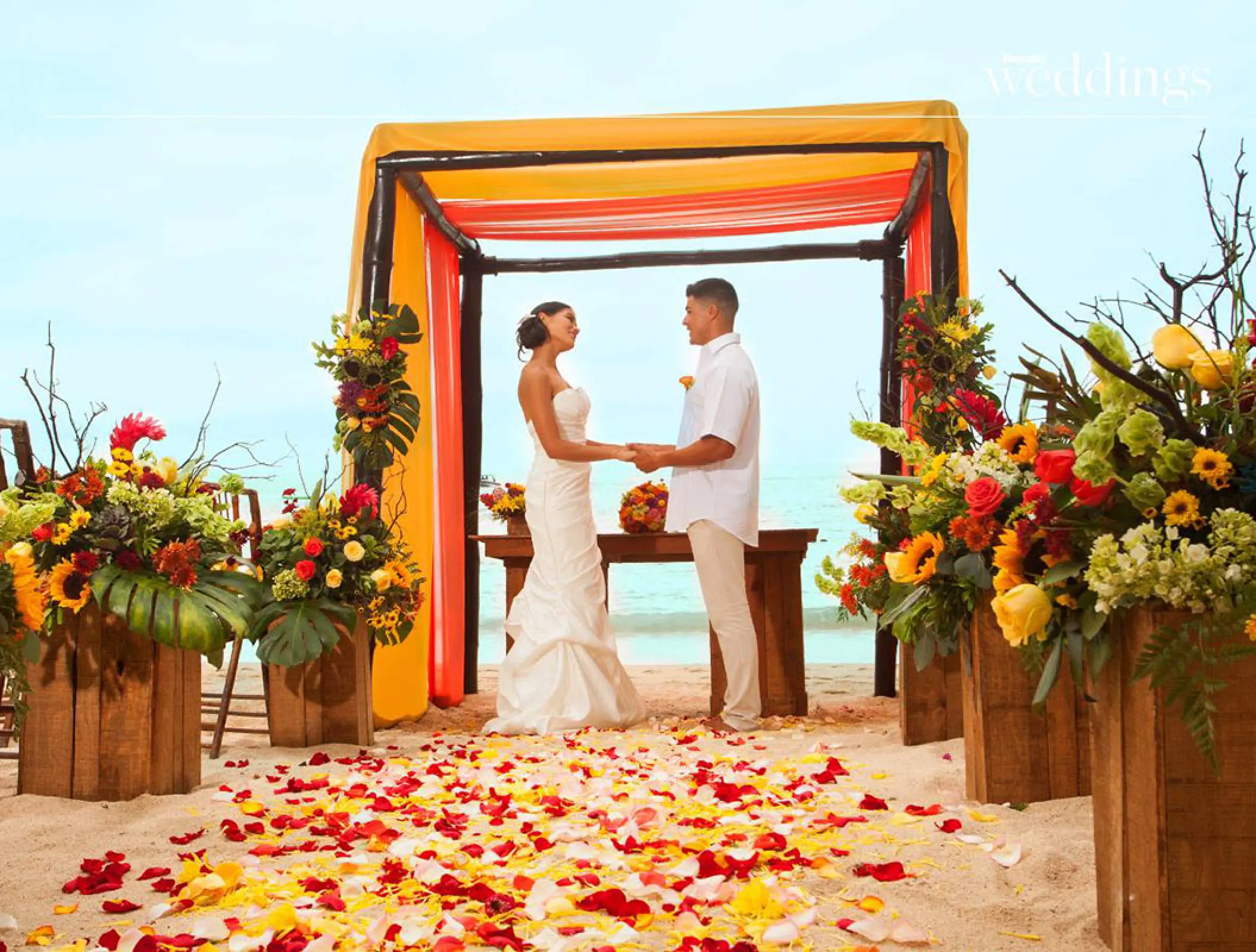 Beachfront wedding ceremony with yellow and orange floral decor at Barcelo Puerto Vallarta