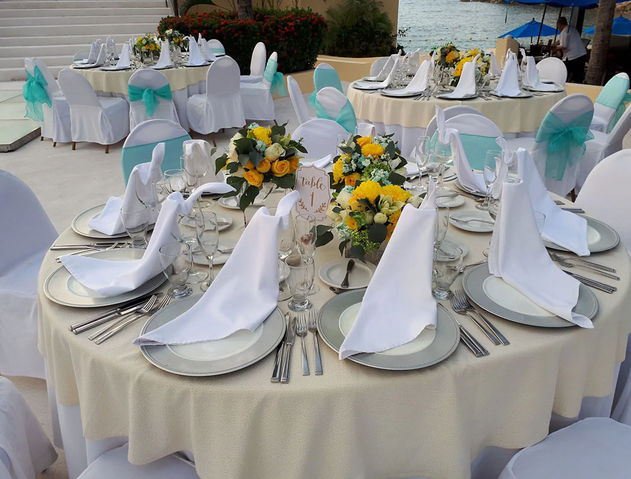 Outdoor wedding reception at Barcelo Puerto Vallarta featuring round tables with teal sashes and yellow floral centerpieces