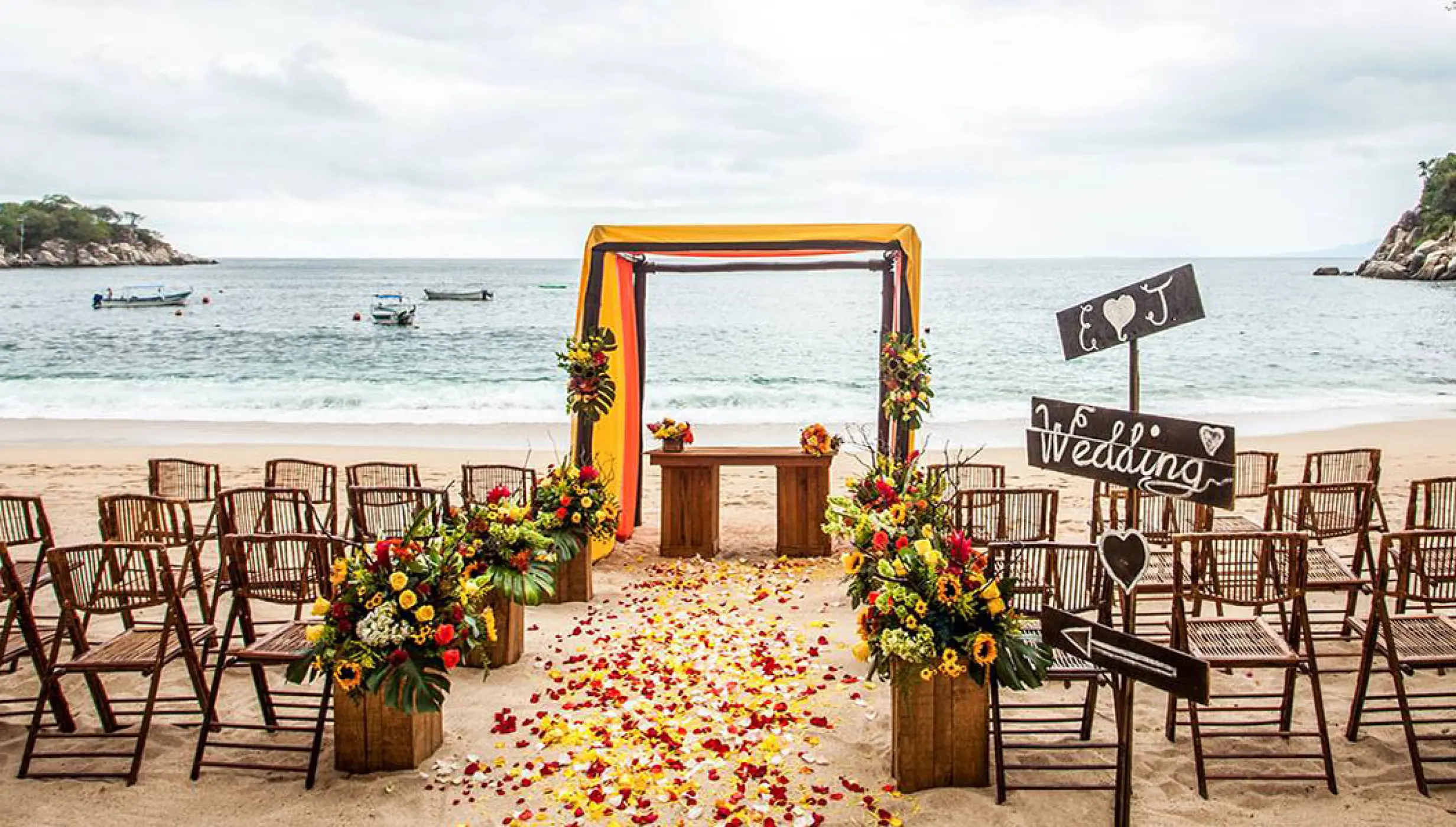 Beach wedding ceremony with floral aisle and wooden chairs at Barcelo Puerto Vallarta