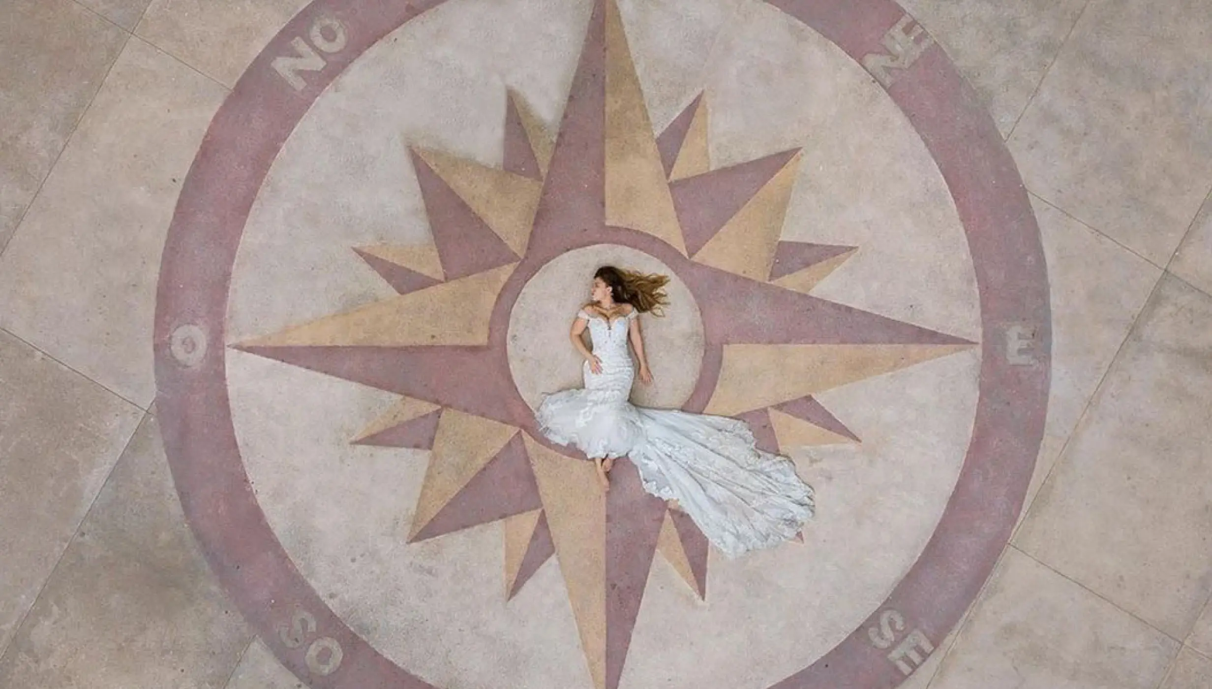 Aerial view of a bride laying in the center of a stone compass at Barcelo Puerto Vallarta