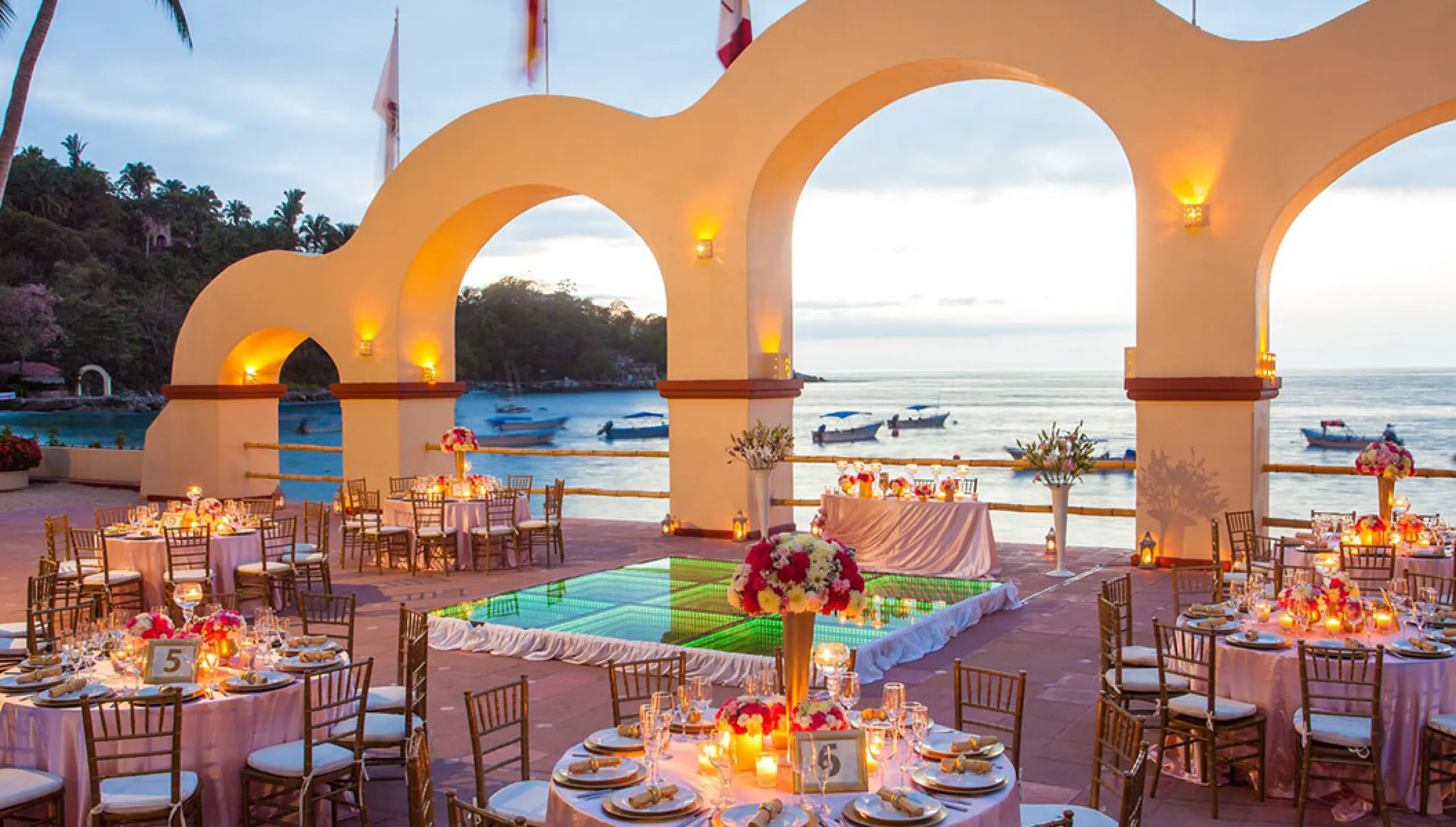 Outdoor wedding reception with an illuminated dance floor under arched columns at Barcelo Puerto Vallarta