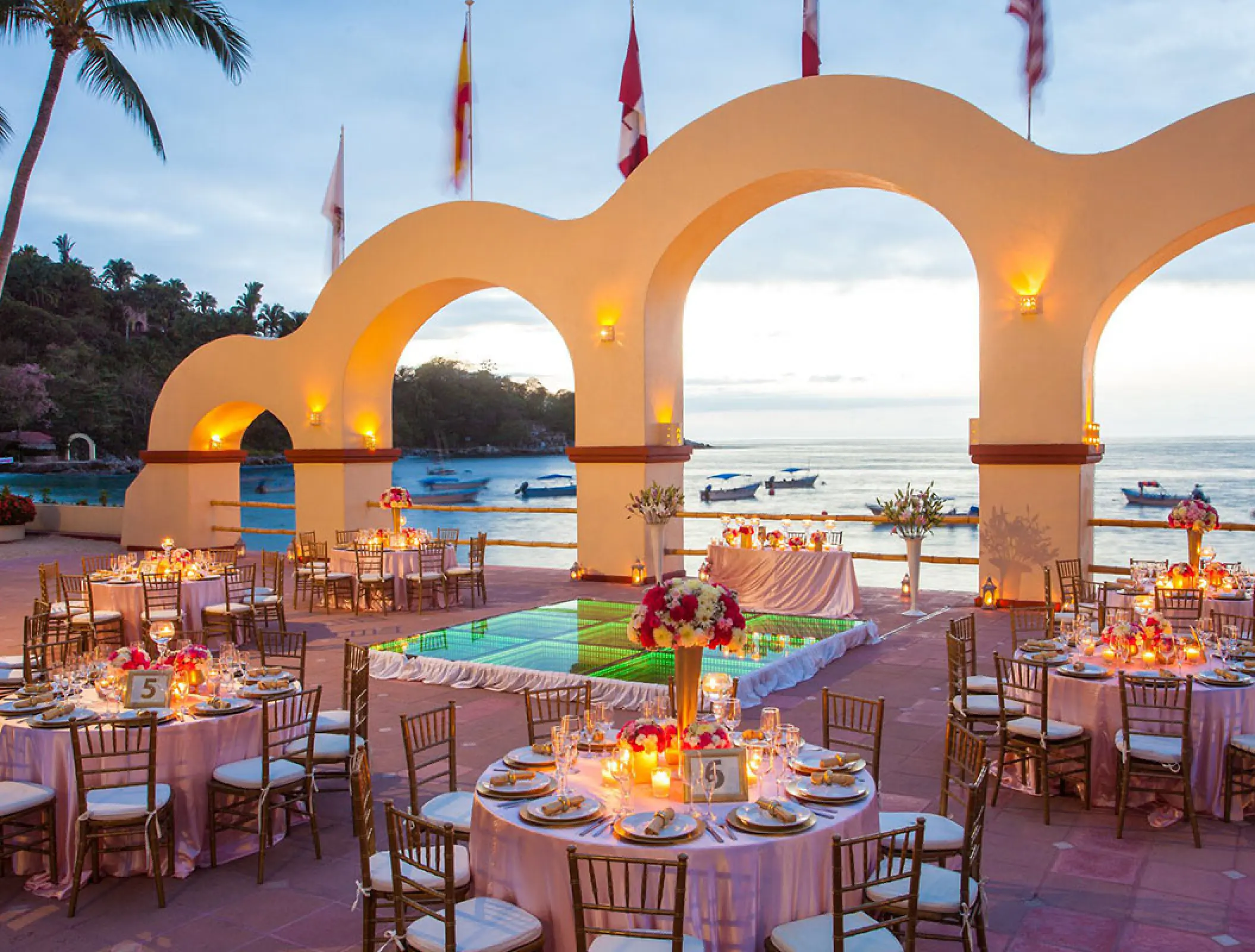 Outdoor wedding reception with an illuminated dance floor under arched columns at Barcelo Puerto Vallarta