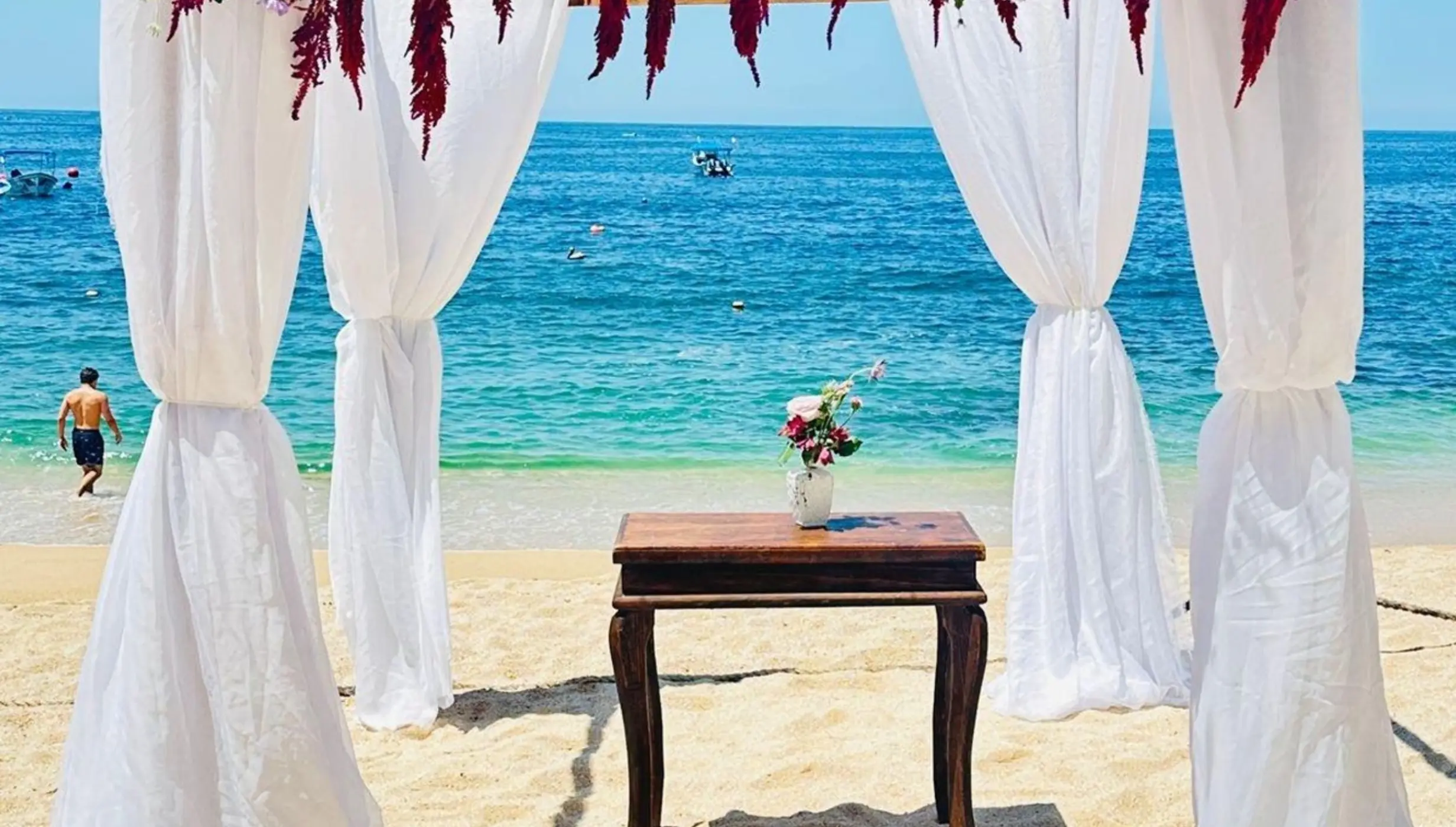 Beach wedding ceremony setup with a floral arch and white fabric at Barcelo Puerto Vallarta