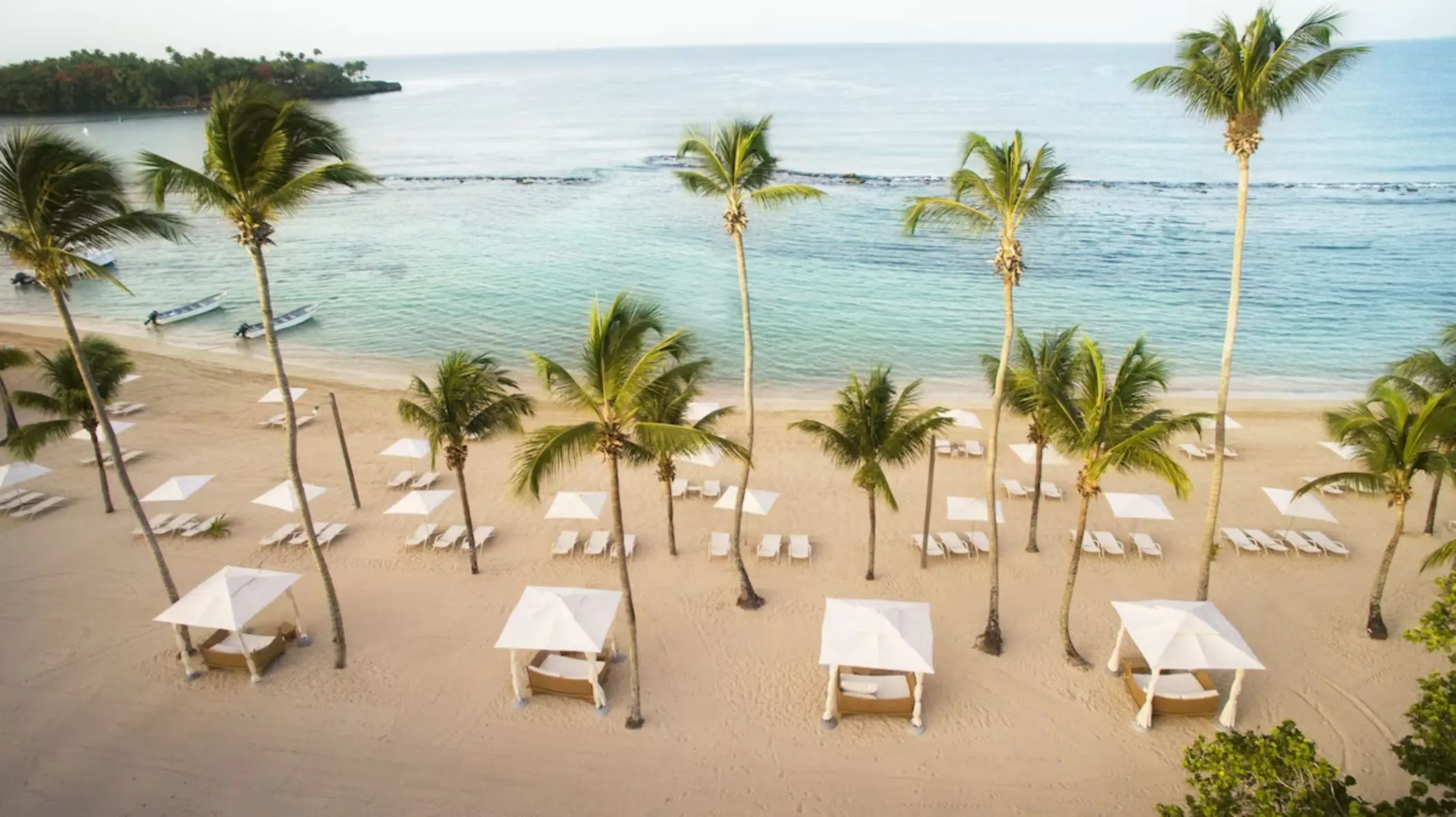 Aerial view of palm trees, white cabanas, and lounge chairs on the beach at Casa de Campo, La Romana