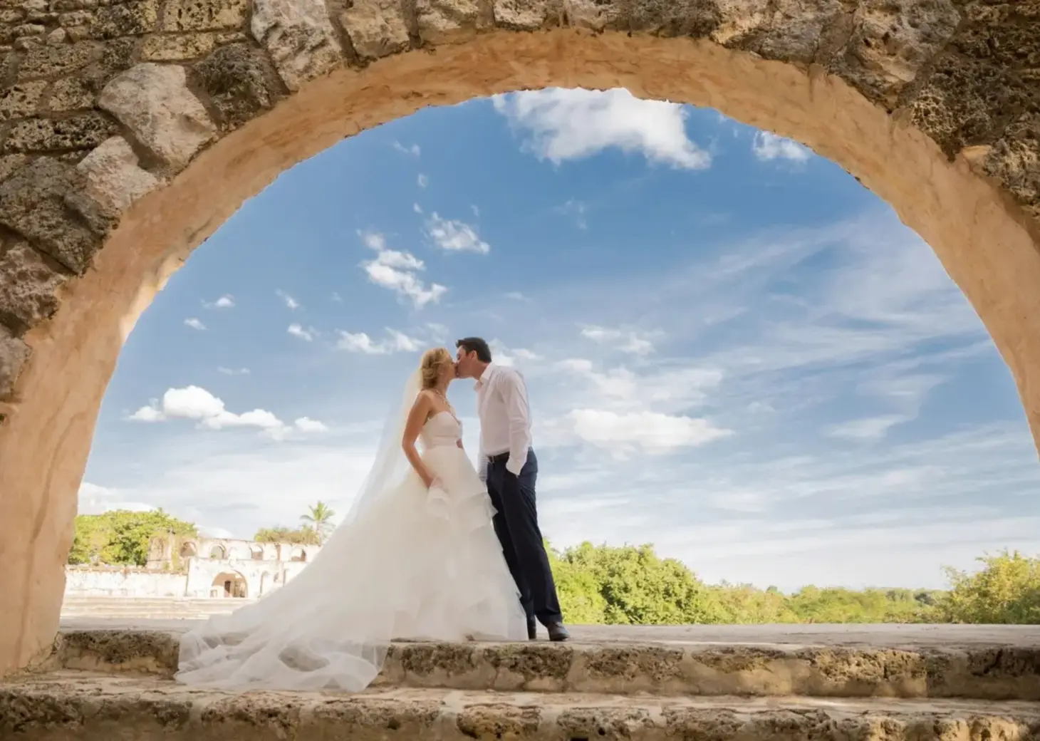 Bride and groom kissing under a stone arch at Casa de Campo, La Romana