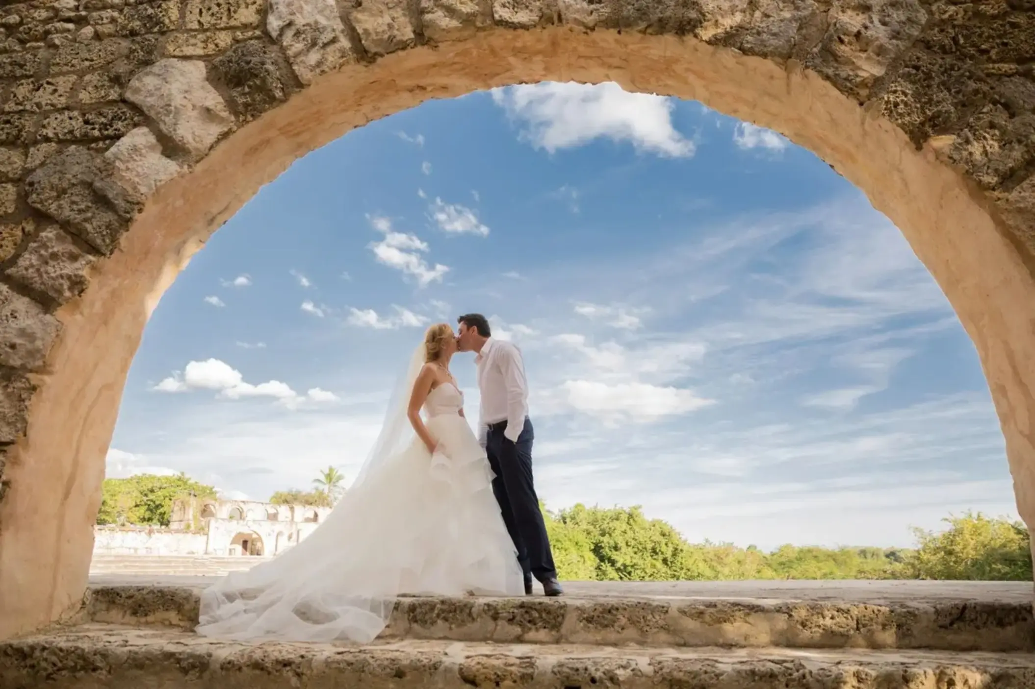 Bride and groom kissing under a stone arch at Casa de Campo, La Romana