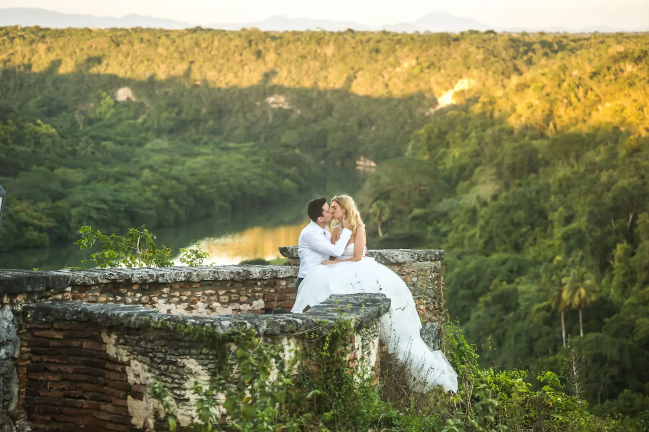 Bride and groom kissing on a stone terrace overlooking the Chavón River at Casa de Campo, La Romana