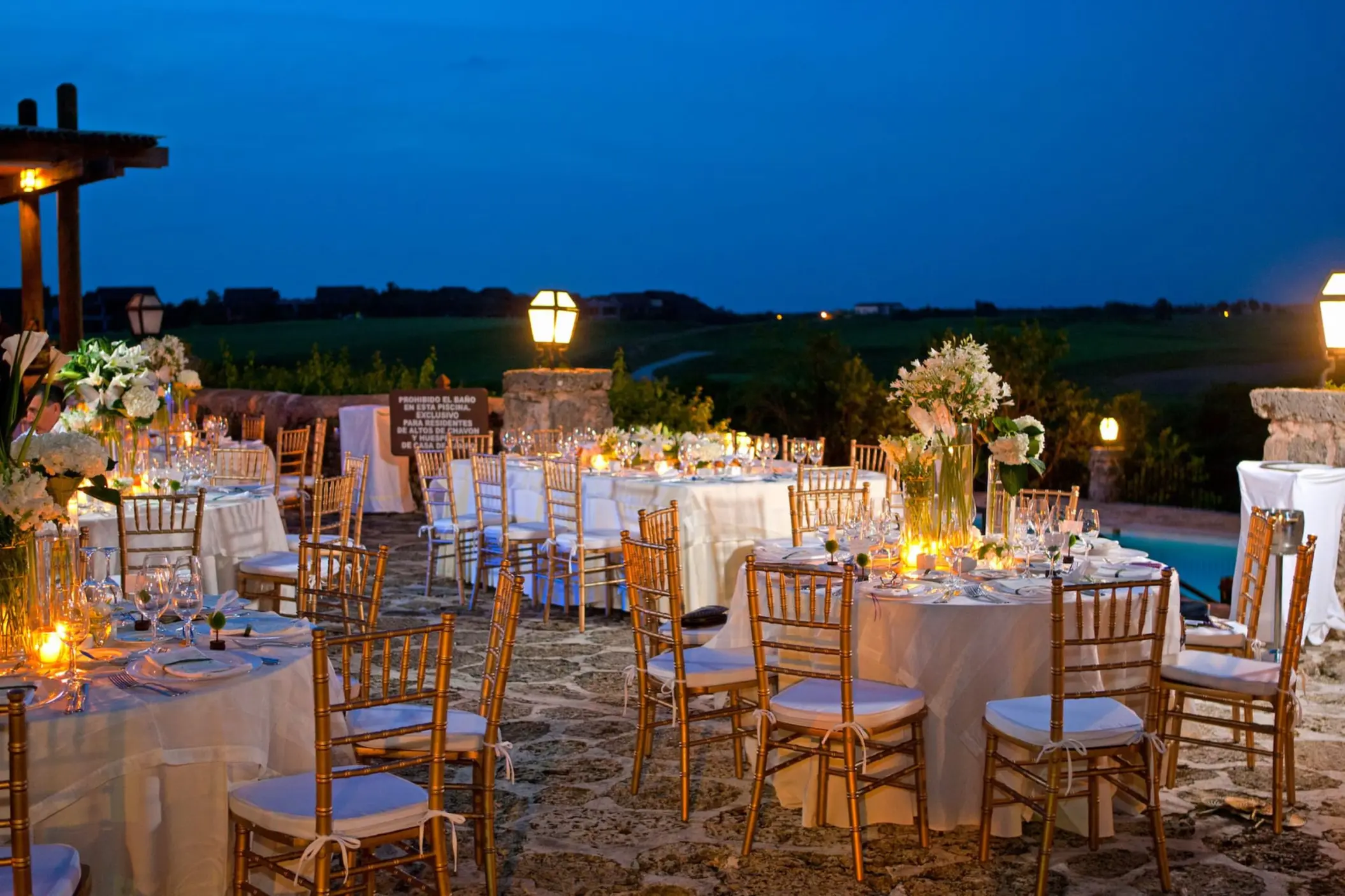 Evening wedding reception terrace with round tables and lit lanterns at Casa de Campo, La Romana