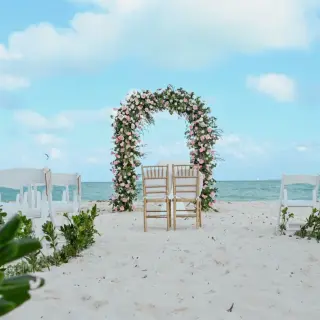 Beachfront wedding ceremony with a floral arch and white chairs at Catalonia Grand Costa Mujeres, Cancun