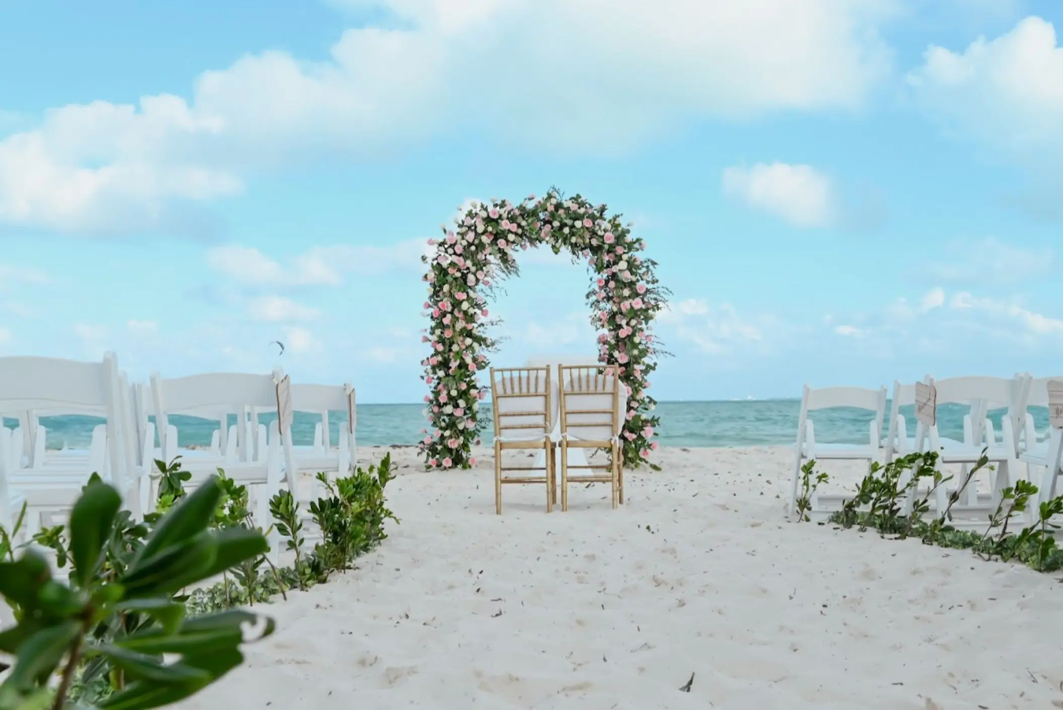 Beachfront wedding ceremony with a floral arch and white chairs at Catalonia Grand Costa Mujeres, Cancun