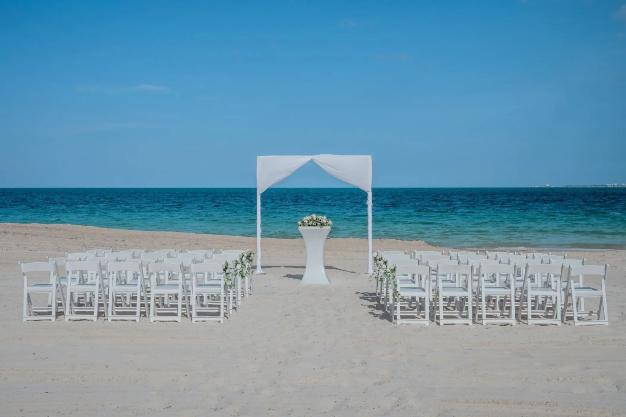 Beach wedding ceremony with a white fabric arch and folding chairs at Catalonia Grand Costa Mujeres, Cancun