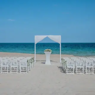 Beach wedding ceremony with a white fabric arch and folding chairs at Catalonia Grand Costa Mujeres, Cancun